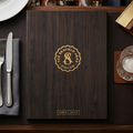 Wooden menu cover with a restaurant logo on a table setting with a glass of water, lemon, and a plate.